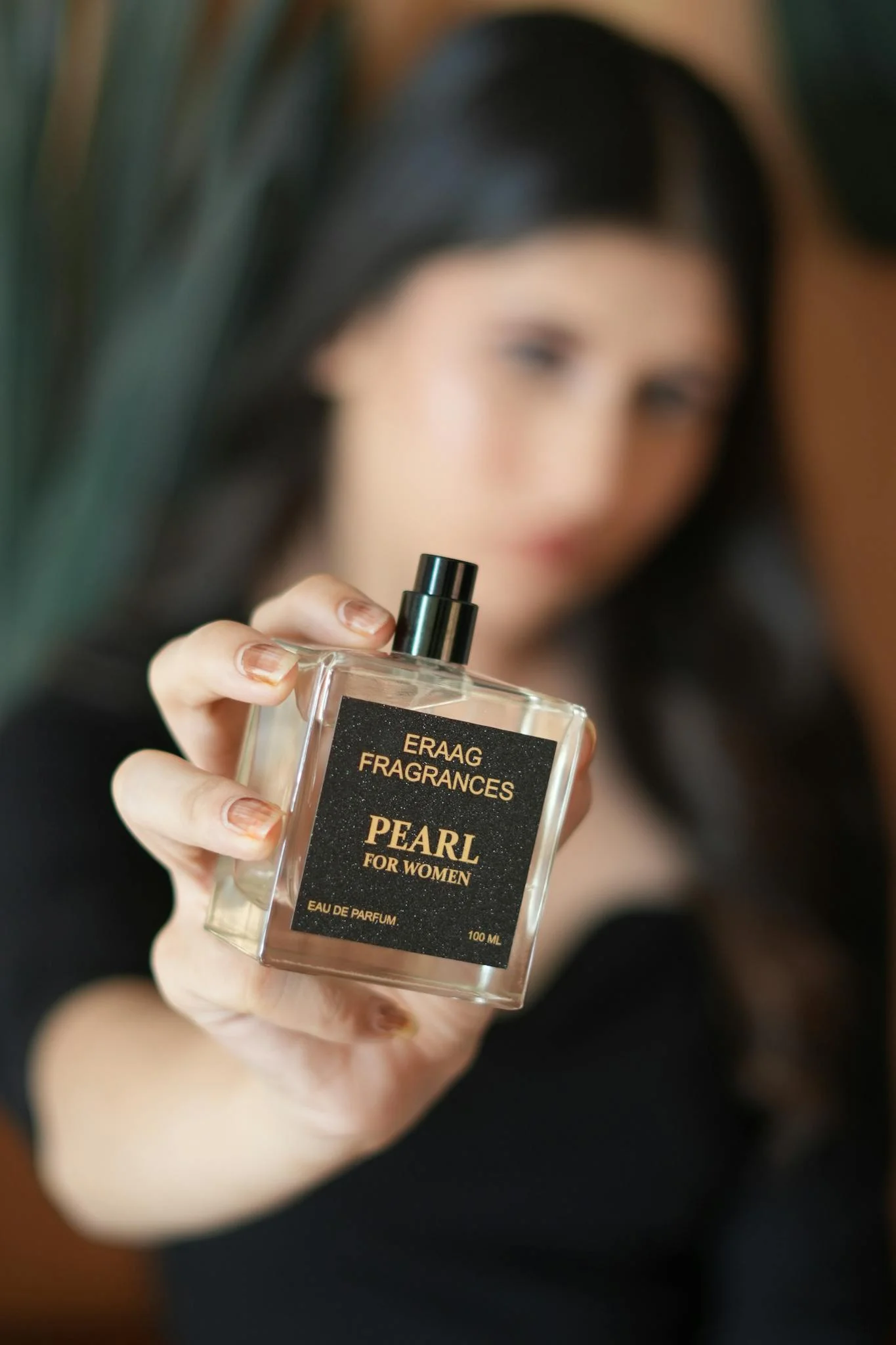 Elegant close-up of a woman holding a luxury perfume bottle labeled 'Pearl' by Eraag Fragrances.
