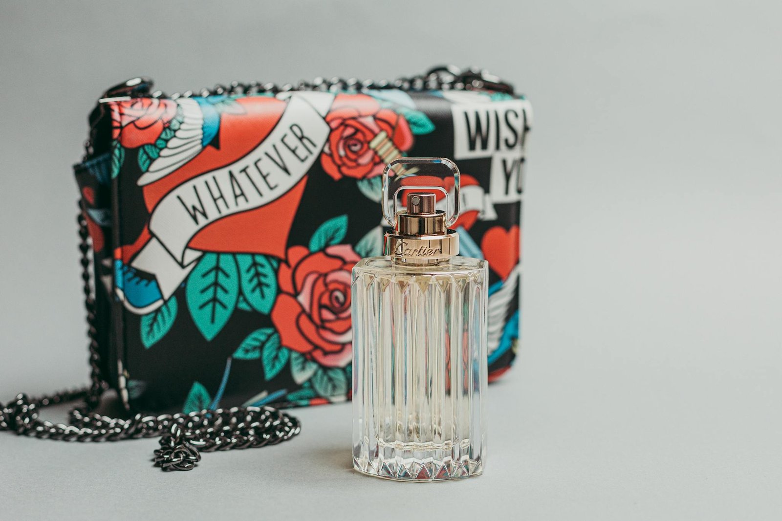 Stylish Cartier perfume bottle and colorful designer bag in a chic flatlay setting.